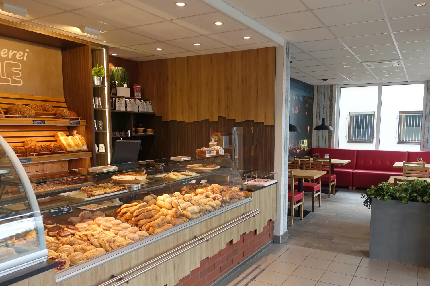 Der Verkaufsraum der Bäckerei Kienzle in der Gaußstraße: eine gefüllte Auslage mit Brötchen, Teilchen und Kuchen, dahinter die Brotregale, rechts der Cafébereich mit roten Sitzbänken